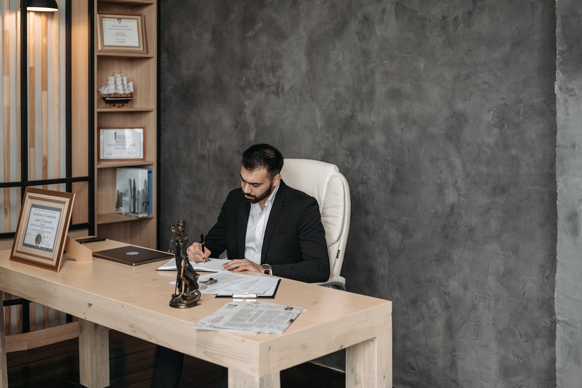 Businessman in a suit writing at a desk in a modern office setting.