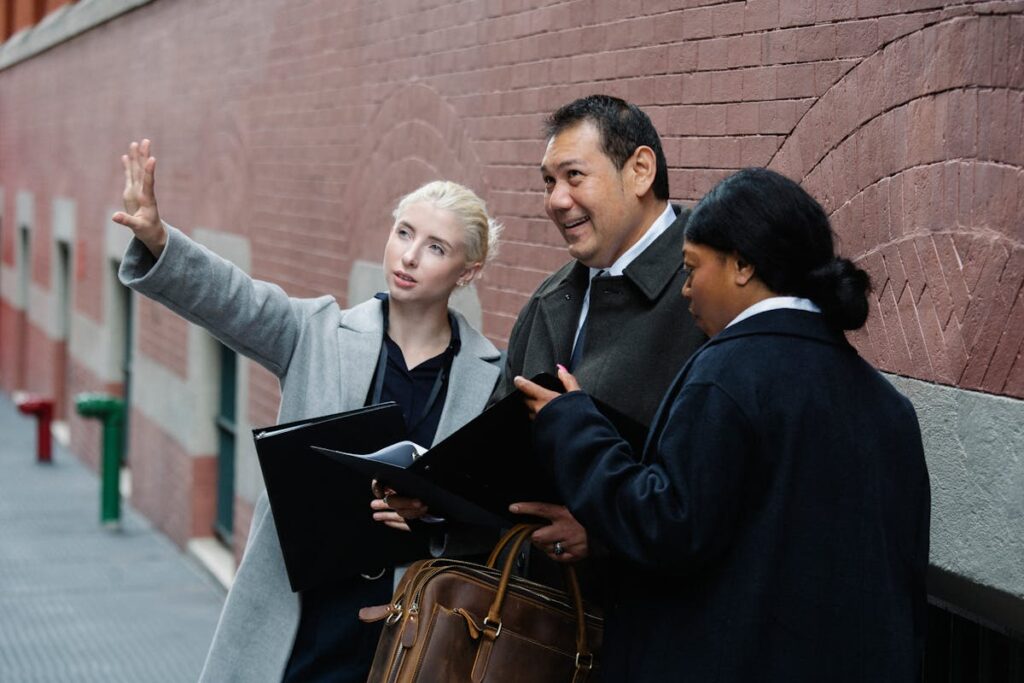 A diverse group of professionals engaged in discussion near a brick wall on the street.